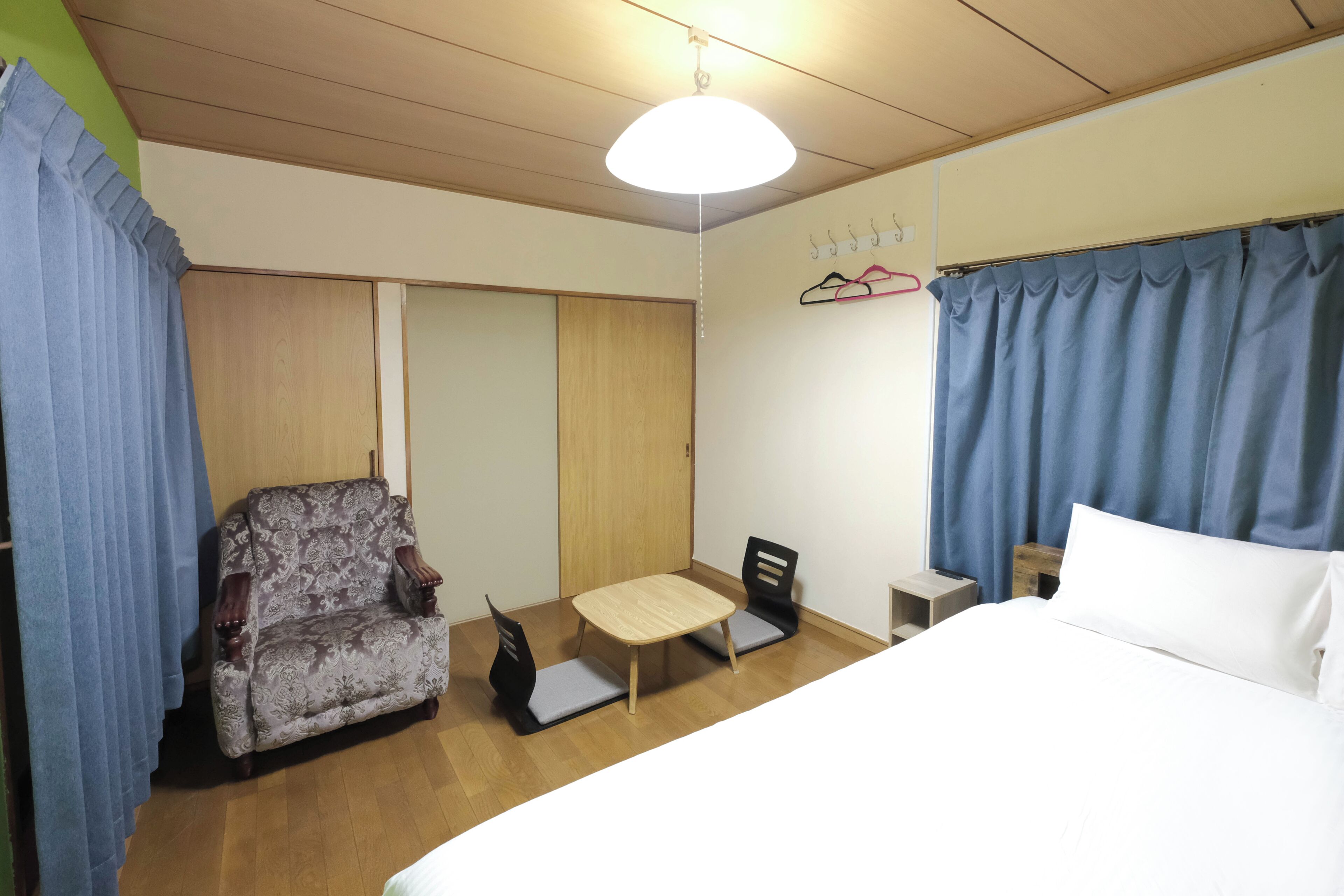 A hotel room with a bed, a chair, a small table, a wardrobe, and a hanging coat rack.