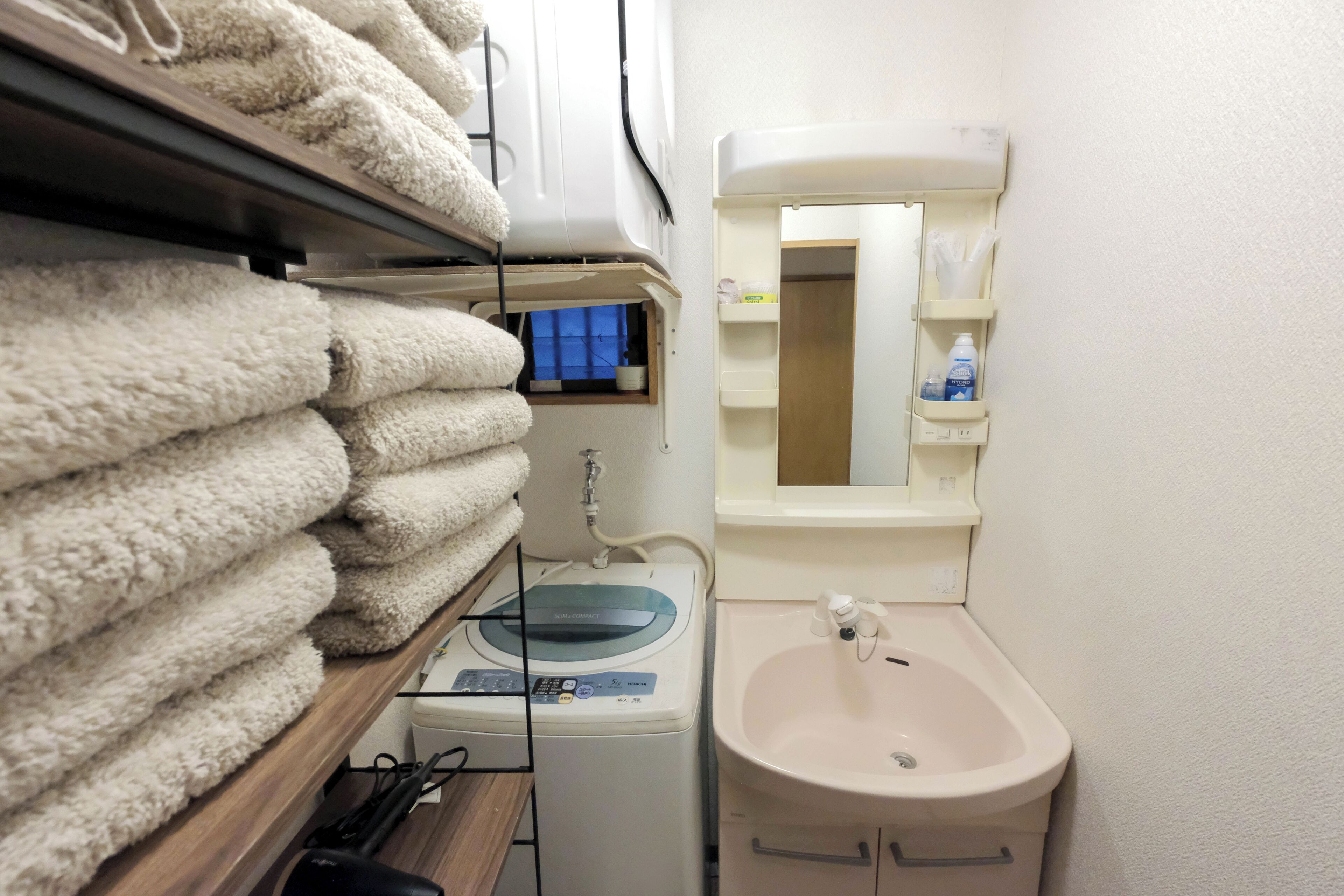 A compact bathroom with a washing machine, a sink, and a mirror.