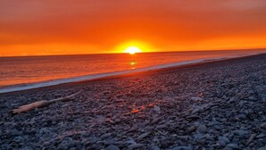 A beach with pebbles and a sunset over the water. - 3-bed gem in Birdlings Flat with stunning lake & ocean views – a rare retreat! (Little River)