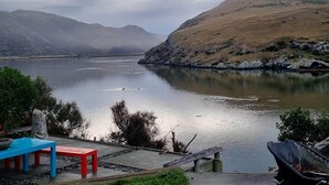 A lakeside view with a bench and a wheelbarrow by the water's edge. - 3-bed gem in Birdlings Flat with stunning lake & ocean views – a rare retreat! (Little River)