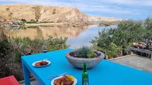 A table with food and a bottle, overlooking a lake and hills. - 3-bed gem in Birdlings Flat with stunning lake & ocean views – a rare retreat! (Little River)