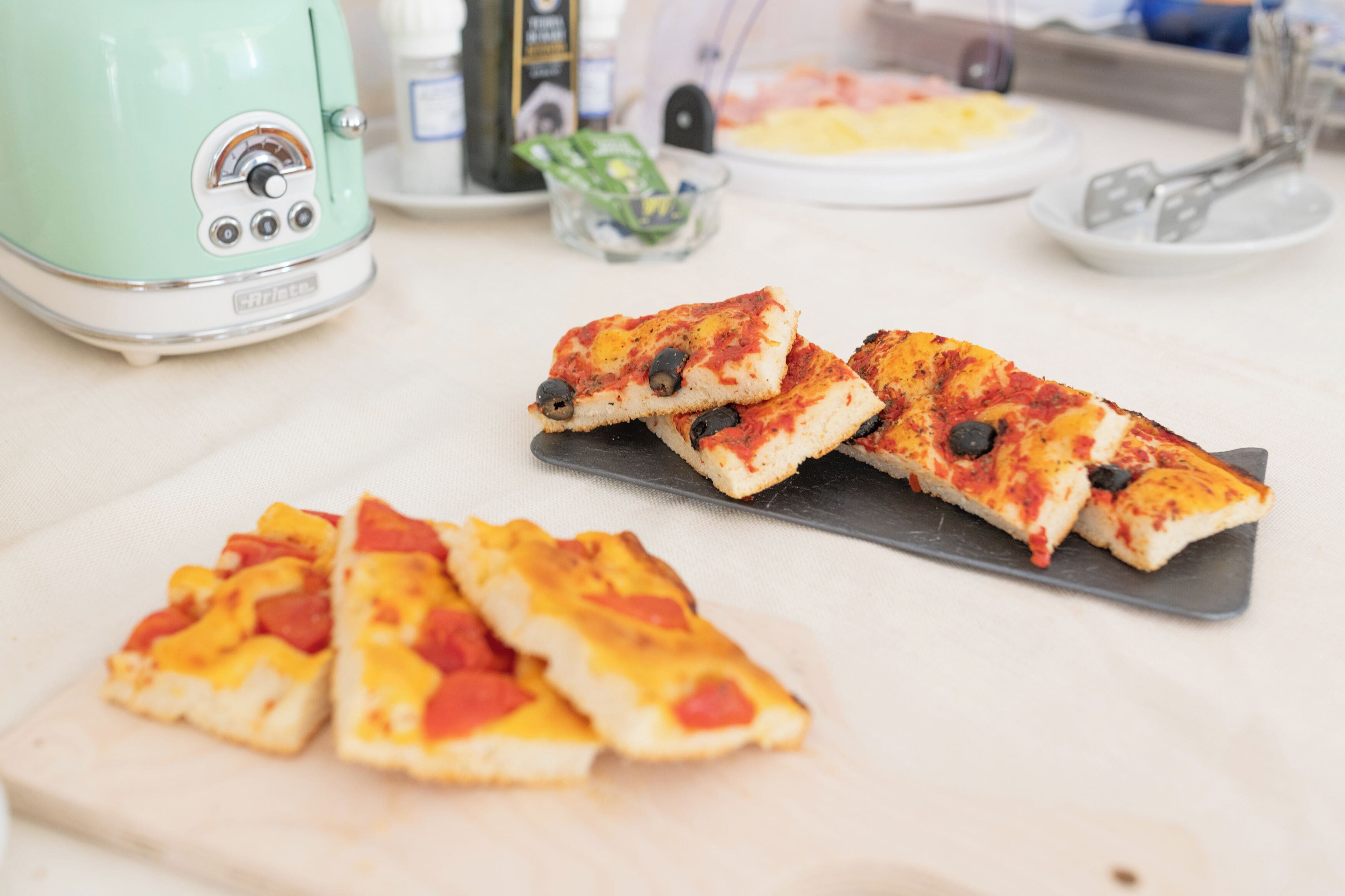 Een keukenblad met een groen apparaat, een snijplank met pizzaslices en een glazen kom met groene inhoud.
