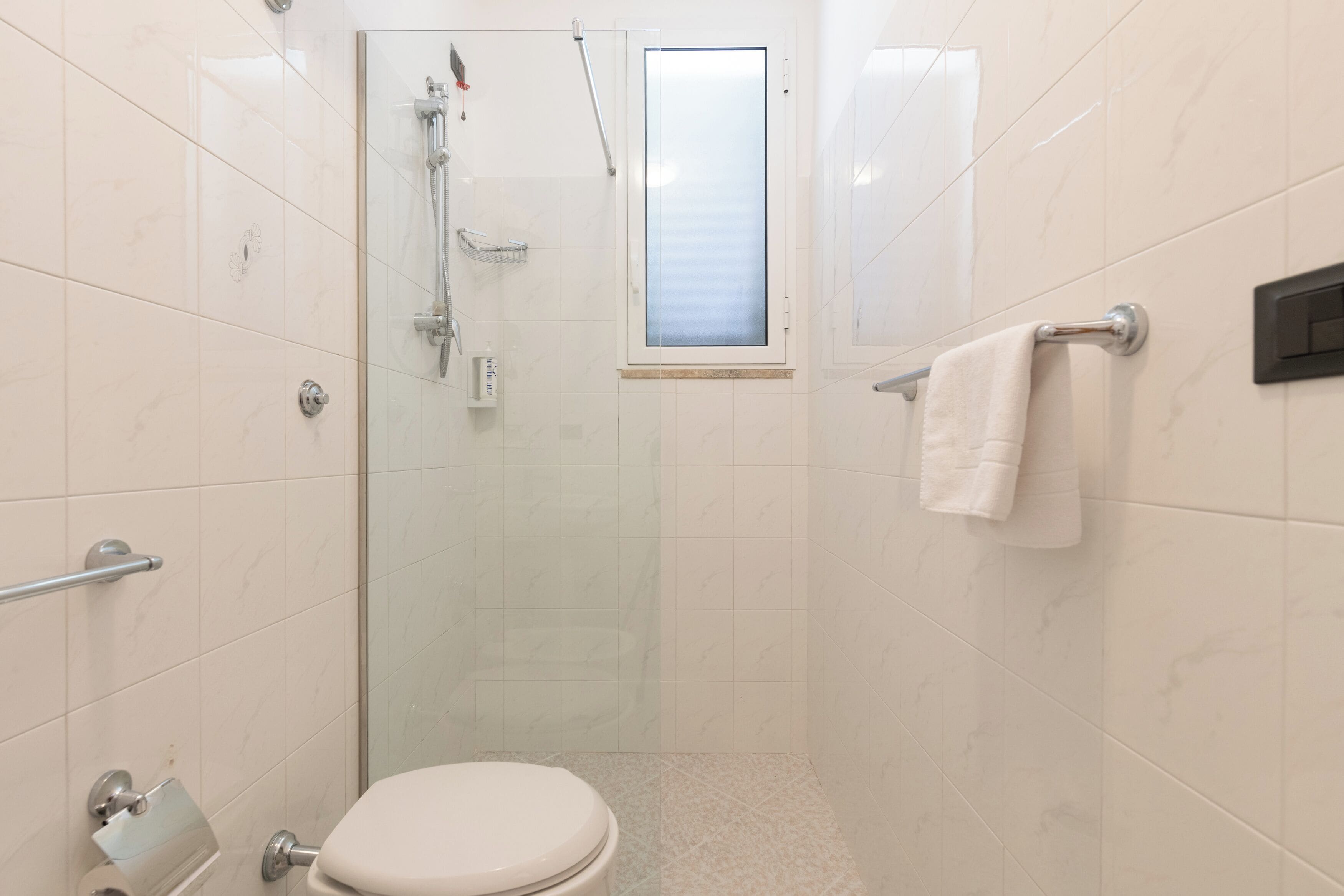 Een moderne badkamer met een douchecabine van glas, een toilet en een handdoekrek.