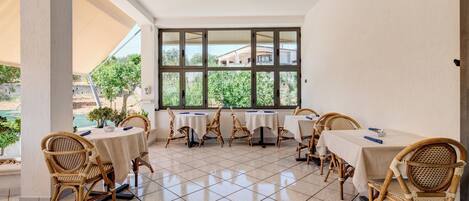 Un espacio de patio techado con mesas y sillas de mimbre, ventanas amplias y un ventilador de techo.
