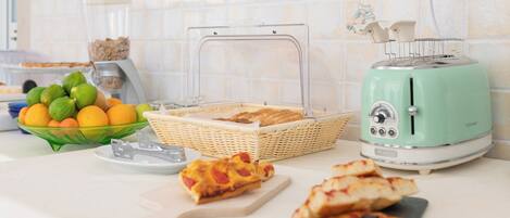 A kitchen counter with a toaster, a bowl of fruit, a basket of bread, and a cutting board with pizza slices.