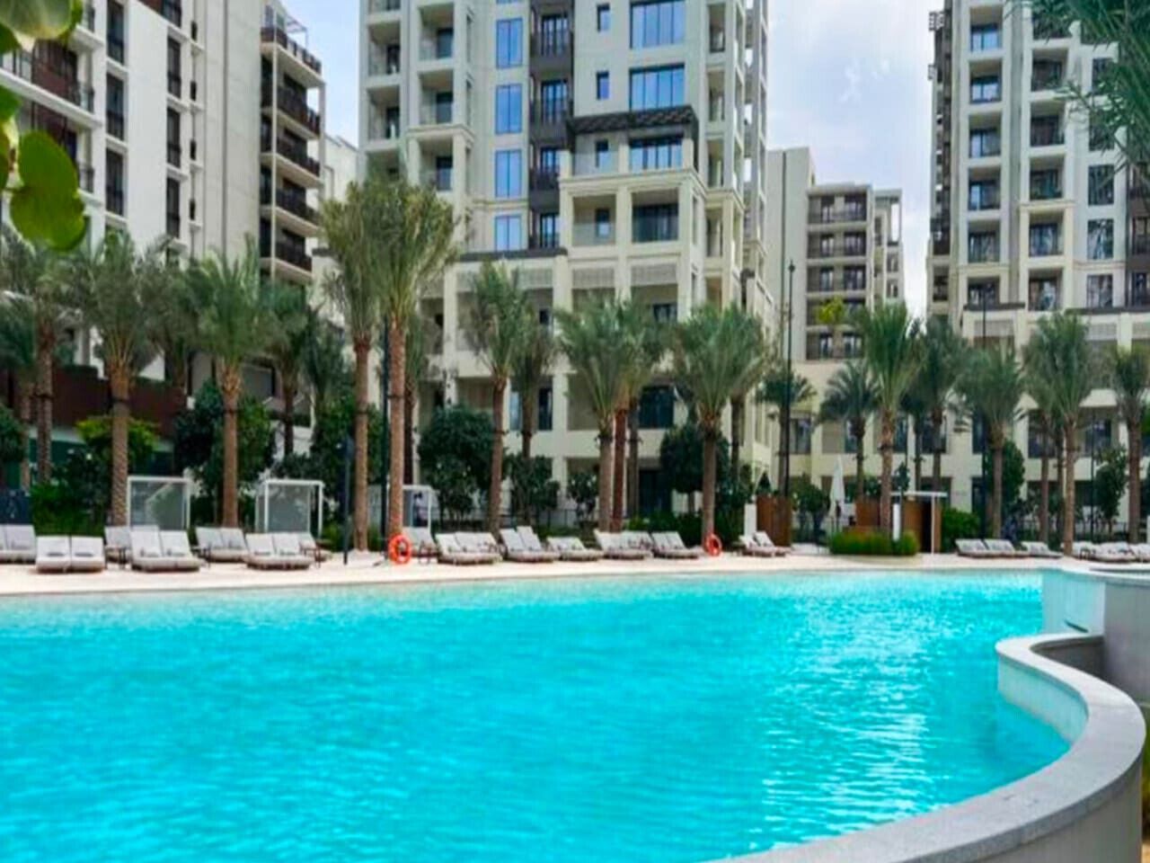 A swimming pool with lounge chairs and palm trees, surrounded by high-rise residential buildings.