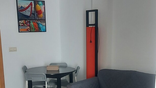 A modern living room with a gray sofa, a black coffee table, and a patterned rug. There is a dining table with chairs and a colorful wall decoration. - ELITE apartment 200 meters from the beach (Cullera)
