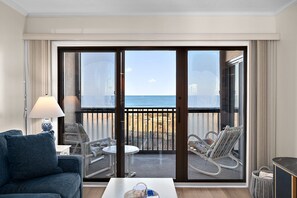 A hotel room with a balcony, a sofa, a table, and a chair.