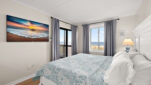 A bedroom with a bed, a window with curtains, a painting of a sunset, and a lamp. - Oceanfront 2 Bed/2 Bath, Sleeps 8 (Ocean City)