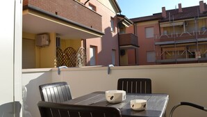 Ein Balkon mit Tisch und Stühlen, der auf ein Wohngebiet mit Backsteingebäuden und hellem Himmel blickt.