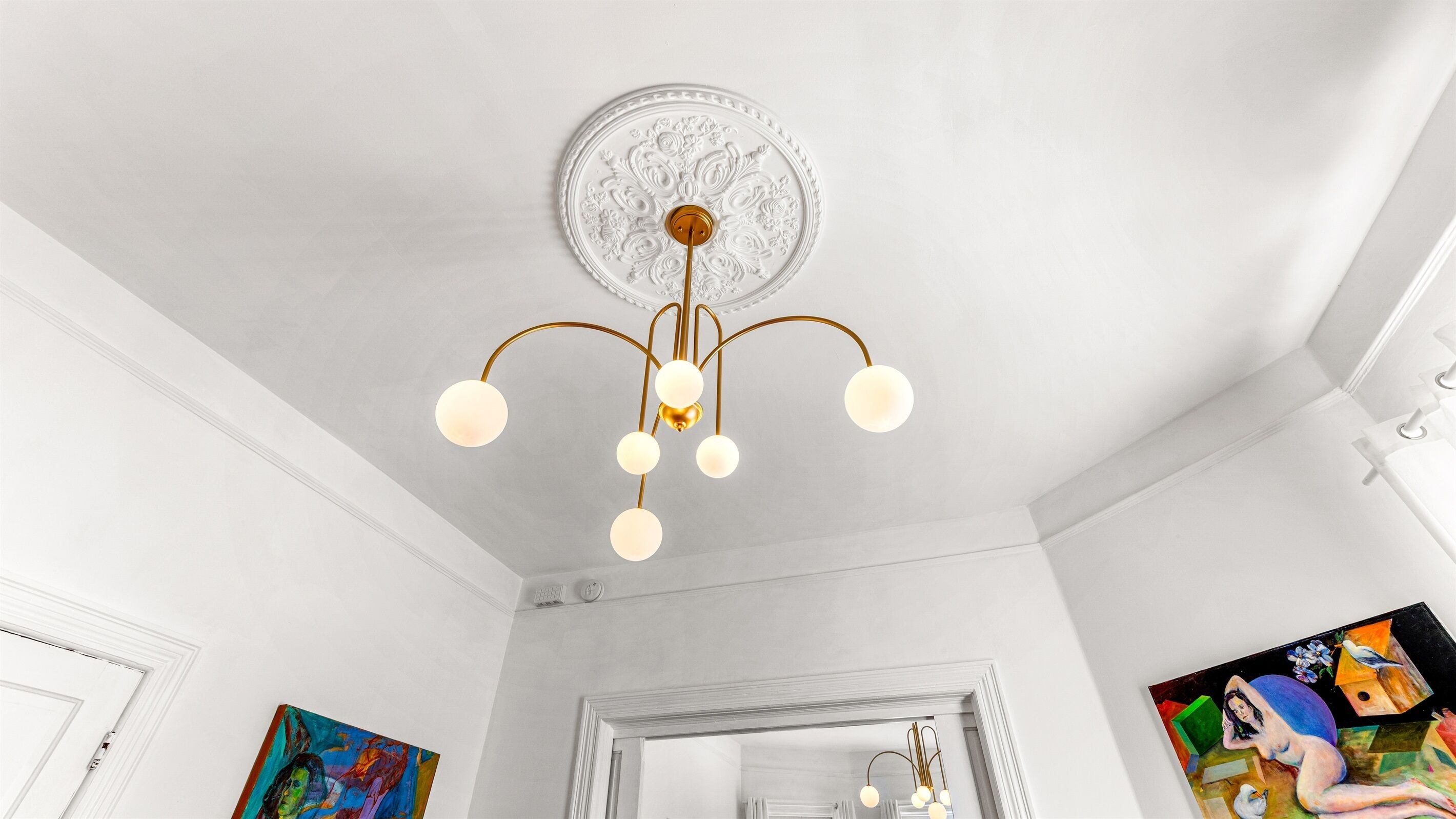 Ein Zimmer mit weißer Decke, einem Chandelier mit mehreren Glühbirnen und einem Gemälde an der Wand.