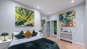 Ein modernes Schlafzimmer mit einem großen Bett, zwei Nachttischen und einer Heizung. An den Wänden befinden sich zwei große abstrakte Gemälde und ein Spiegel, der den Raum reflektiert.