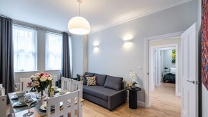 Ein modernes Wohnzimmer mit einem grauen Sofa, einem Esstisch für vier Personen und einem kleinen Beistelltisch mit Blumen.