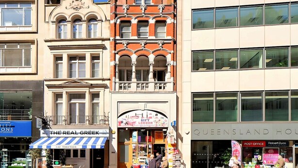 A building with a shop named 'The Real Greek' on the ground floor, a post office on the right, and a Queensland House sign above the post office.