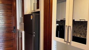 A modern kitchen with a built-in black refrigerator, white cabinets, and a wooden door. - Apartment with garden view (Tambon Karon)