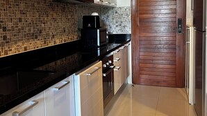 A modern kitchen with white cabinets, a black countertop, and a tiled backsplash. - Apartment with garden view (Tambon Karon)