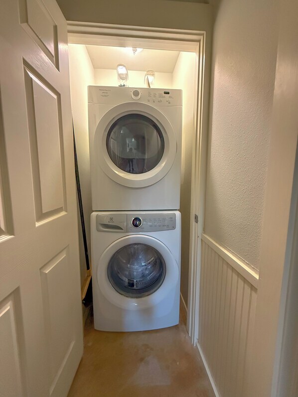 A laundry room with two stacked front-loading washing machines and a dryer, with a door leading into the room.