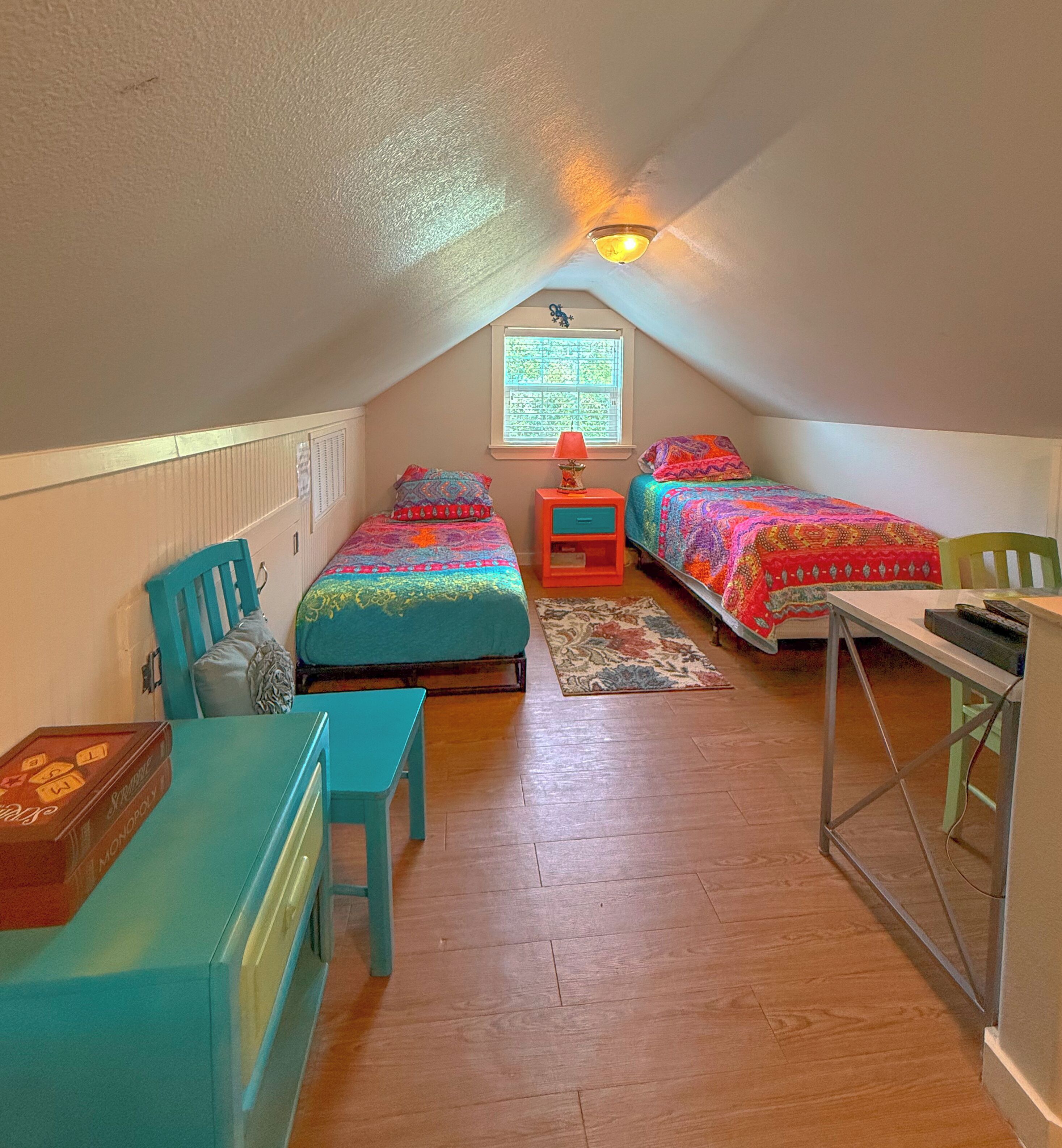 A cozy attic bedroom with two beds, a desk, and a chair.