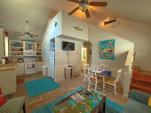 A compact kitchen with a microwave, refrigerator, and wooden cabinets. There is a dining area with a table and chairs, and a ceiling fan.