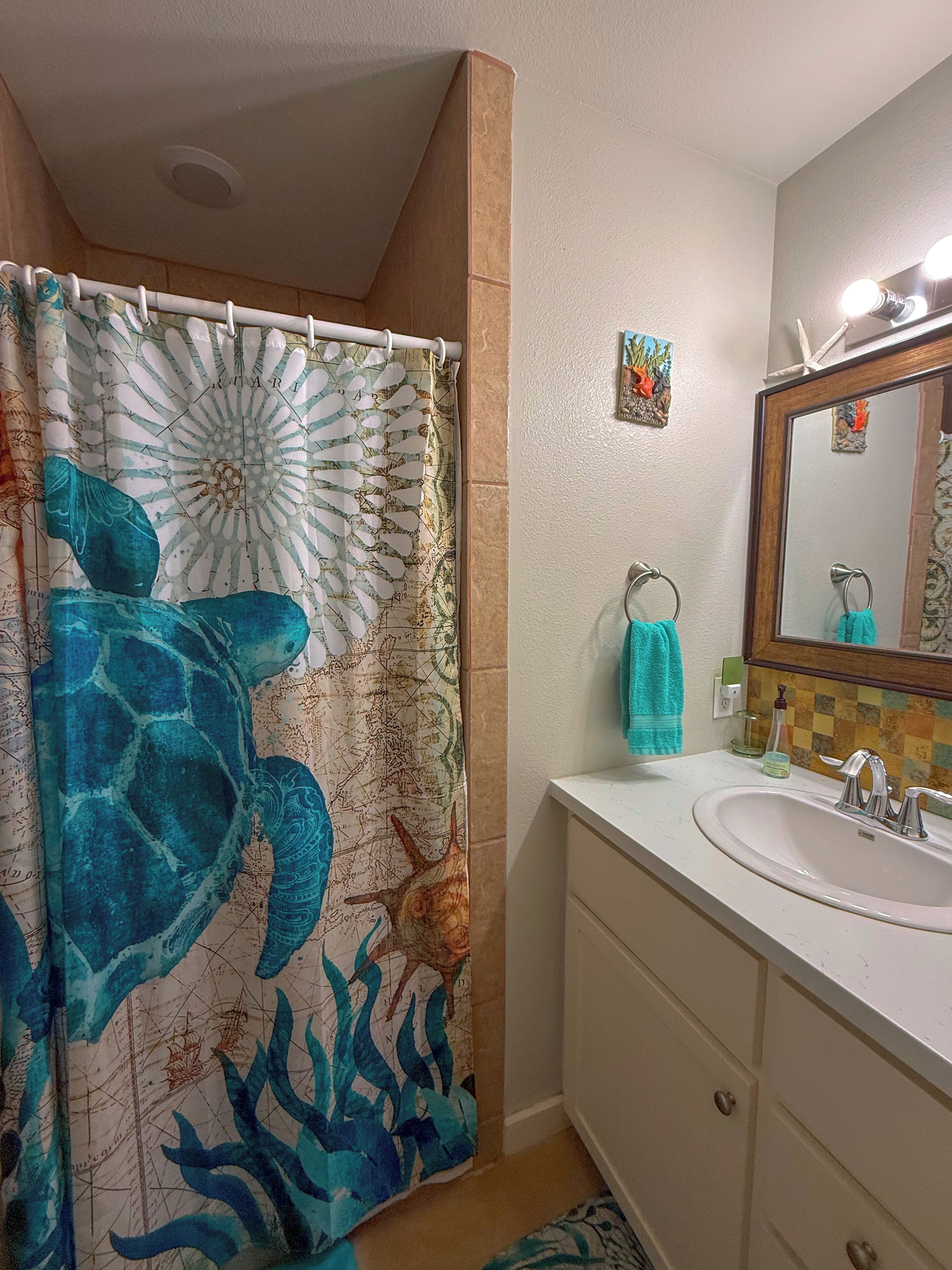 A bathroom with a shower curtain featuring a marine design, a sink with a mirror, and a small decorative item on the wall.