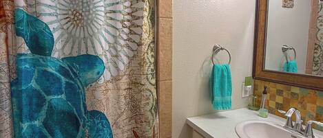A bathroom with a shower curtain featuring a marine design, a sink with a mirror, and a small decorative item on the wall.