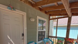 Une véranda couverte avec des poutres en bois, une porte blanche et des chaises turquoise avec des coussins.