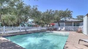 Une piscine avec une terrasse en bois, une clôture blanche en piquets et un espace salon extérieur.
