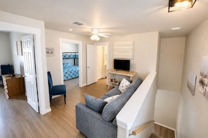 Ein modernes Wohnzimmer mit einer Couch, einem Fernseher und einem Deckenventilator.