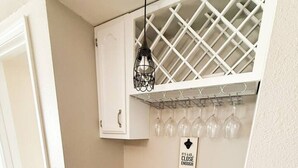 A compact kitchen with a granite countertop, stainless steel sink, white cabinetry, and a wine rack above the sink. - Lakefront Luxury 2BD/2BA Condo at The Falls-7PP (Lake Ozark)