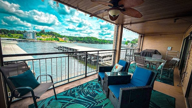 A balcony with a view of a body of water, wicker furniture, and a ceiling fan. - Lakefront Luxury 2BD/2BA Condo at The Falls-7PP (Lake Ozark)