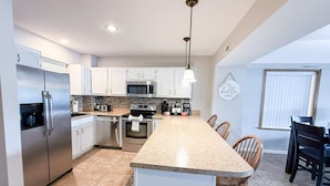 A modern kitchen with stainless steel appliances, a granite countertop, and a dining area with wooden chairs. - Lakefront Luxury 2BD/2BA Condo at The Falls-7PP (Lake Ozark)