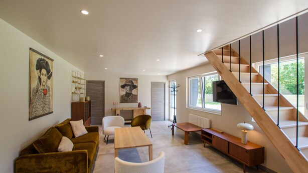 Una sala de estar moderna con una escalera, un sofá, una mesa de centro y un televisor montado en la pared.