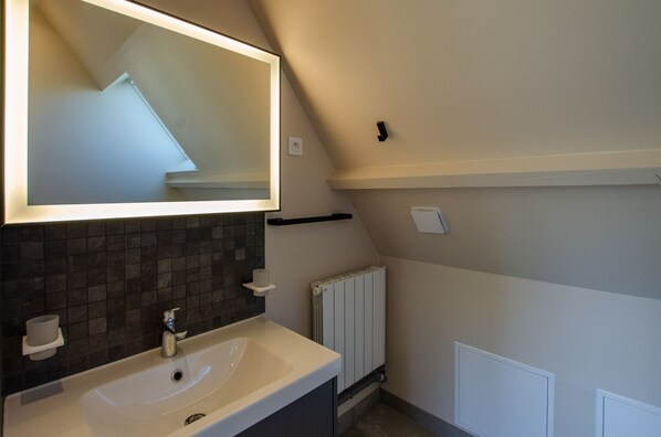 A bathroom with a white sink, dark tiled backsplash, a large mirror, and a white radiator.