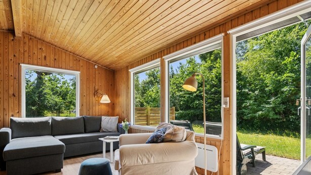 Una habitación acogedora con sofá, reposapiés y cama, ventanas amplias y techo de madera.