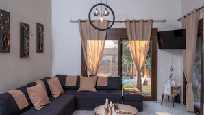 A modern living room with a sectional sofa, a round coffee table with candles, and a view of the outdoors through large windows.