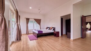 A bedroom with a bed, a nightstand, a window with curtains, and a door leading to another room. - Priyas Villa Vagamon by VOYE HOMES (Peermade)