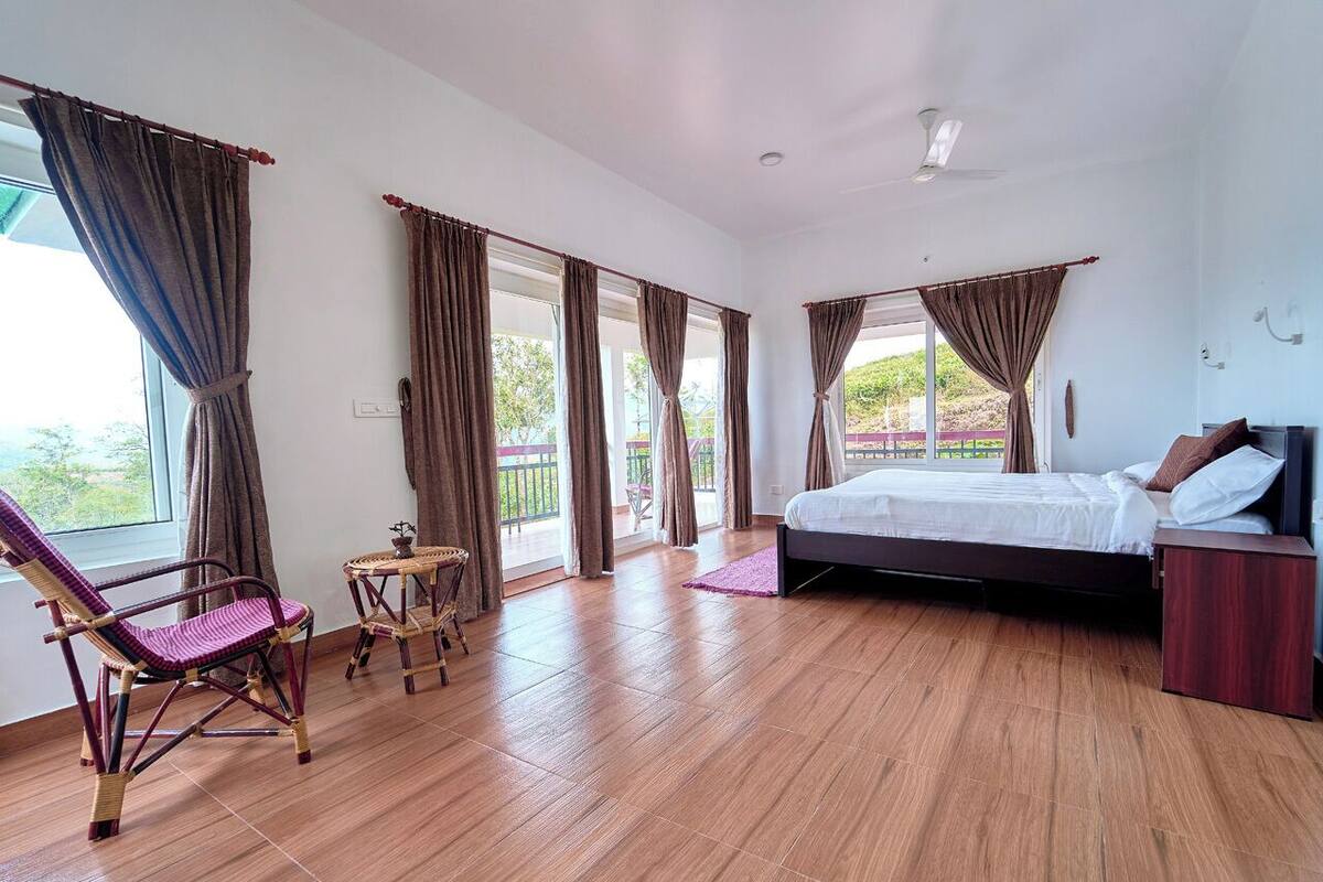 Une chambre à coucher avec un lit, une chaise, une petite table et une fenêtre avec des rideaux.