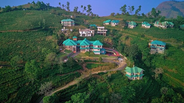 A hillside tea plantation with several houses with green roofs. - Priyas Villa Vagamon by VOYE HOMES (Peermade)