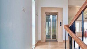 A modern interior with a wooden staircase, a glass elevator, and a plain wall. - Priyas Villa Vagamon by VOYE HOMES (Peermade)