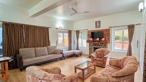 A spacious living room with a sofa set, armchairs, a coffee table, and a fireplace. - Priyas Villa Vagamon by VOYE HOMES (Peermade)