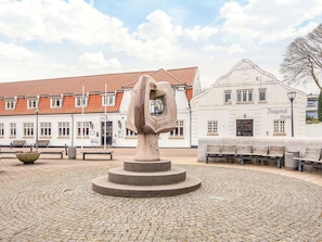 A cobblestone plaza with a stone sculpture, benches, and a building with a tiled roof. - 4 Person Holiday Park Home in Give (Give)