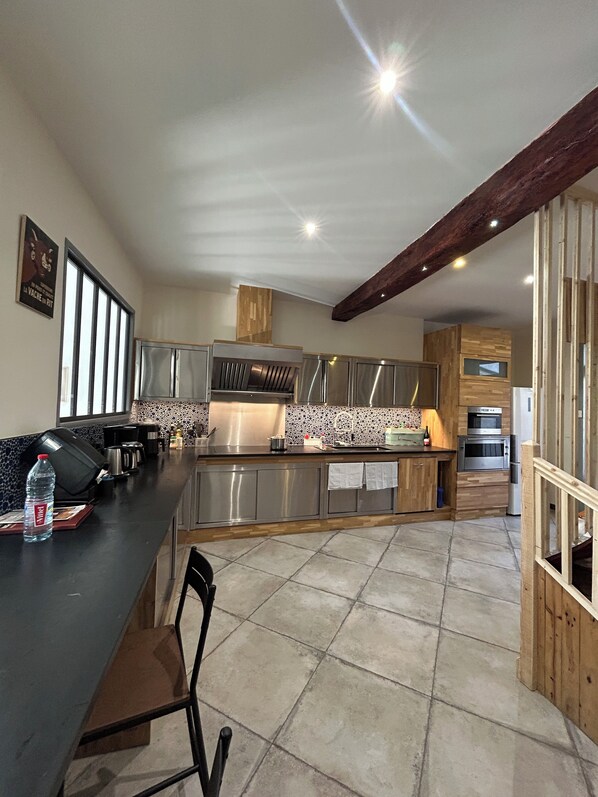 A modern kitchen with a central island, stainless steel appliances, and a wooden ceiling beam.