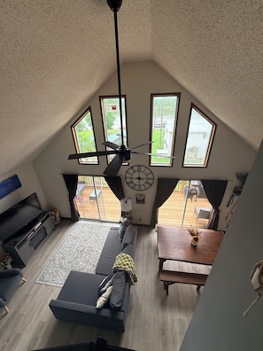 A loft-style room with a ceiling fan, a clock, and a view of a wooden deck through large windows. - Digital Detox Cabin, Wi-Fi hotspot available for add on, Boat Ramp access across the street (Roach)