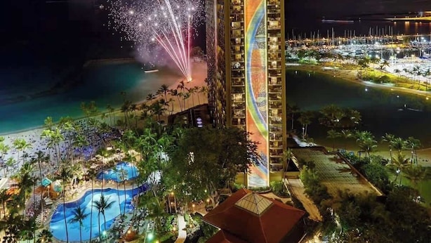 Un hotel con piscina, rodeado por una playa y palmeras.