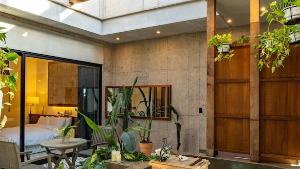 Une chambre d’hôtel moderne dotée d’une grande verrière, d’une porte en bois et d’un balcon agrémenté de plantes.