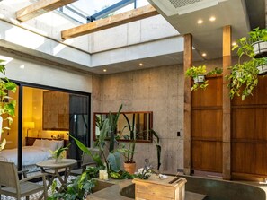 A modern hotel room with a large skylight, a wooden door, and a balcony with plants.