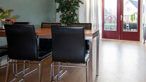 Un comedor con una mesa de madera, cuatro sillas negras, dos lámparas colgantes y una planta en maceta.