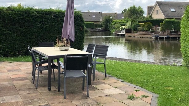 Un patio con una mesa y sillas, una planta en maceta y vistas a un canal con casas al fondo.
