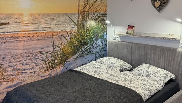 Ein Schlafzimmer mit einem großen Bett, einer Wandleuchte und Blick auf den Strand.