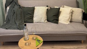 Ein Wohnzimmer mit grauem Sofa, einer grünen Decke, einer Weinflasche und einem Glas auf einem kleinen Holztisch.